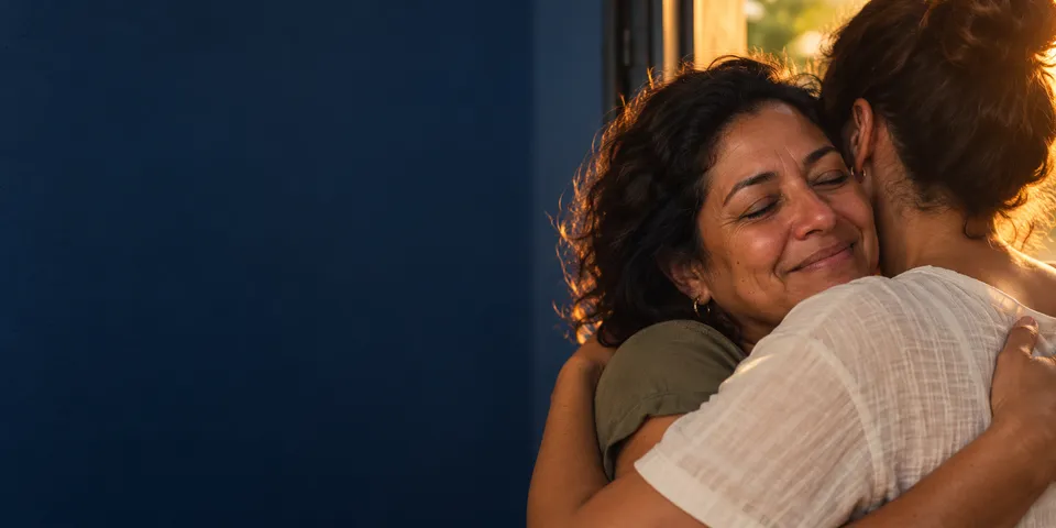 Duas mulheres se abraçam com alegria e emoção, de olhos fechados, à luz dourada do fim de tarde.